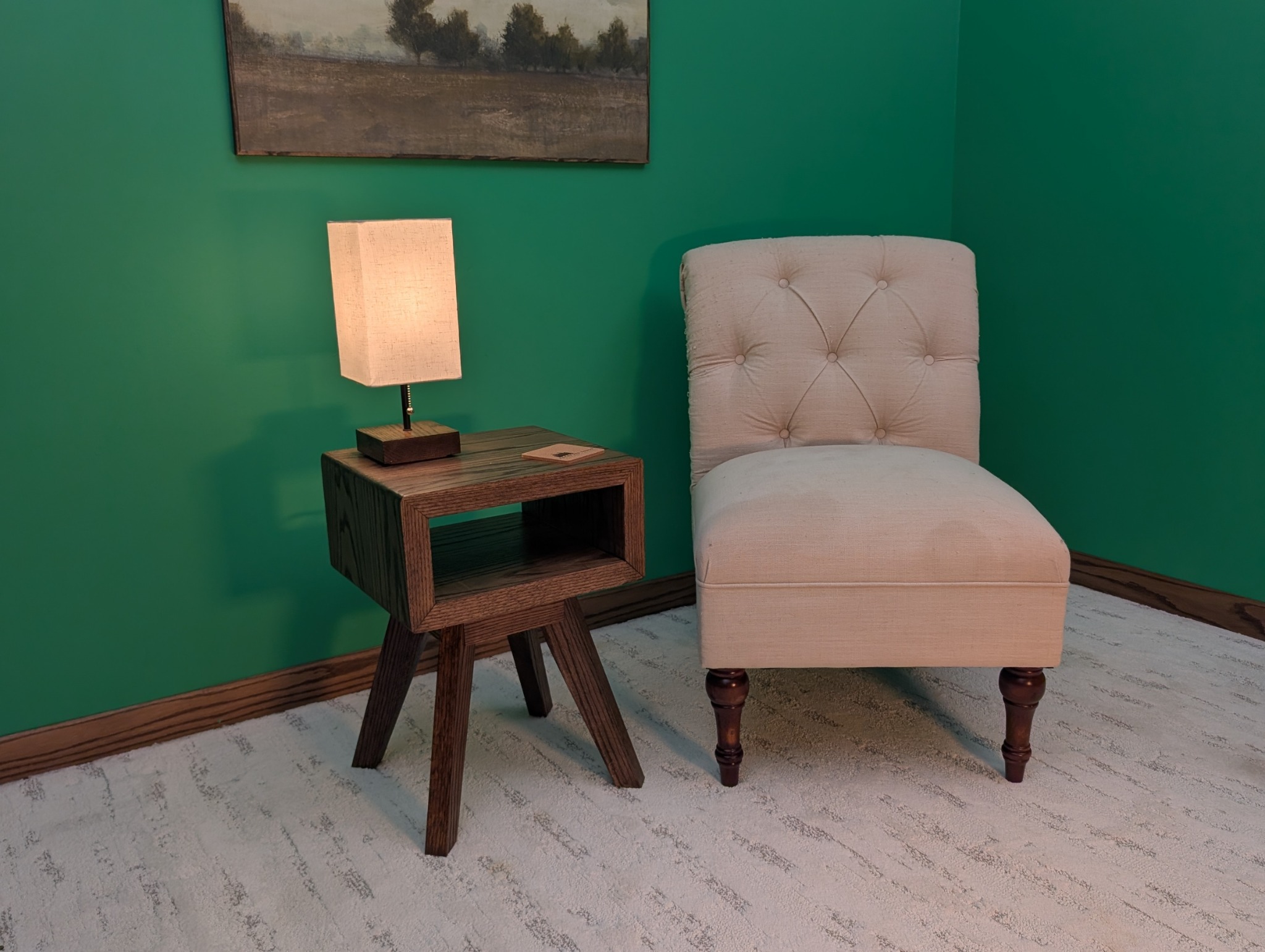 Oak chairside table with a lit lamp beside an upholstered reading chair